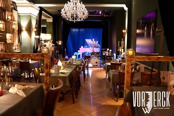 Eventlocation: Der Blick vom Podest zur Bühne, mit eingedeckten Tischen für einen Firmenevent. - Restaurant Vorwerck